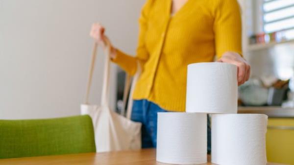 A young woman is taking out toilet papers from a reusable shopping bag at home.